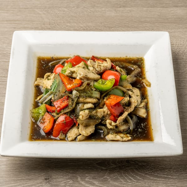 Thai basil chicken with red and green bell peppers, onions, and a savory sauce on a white plate.