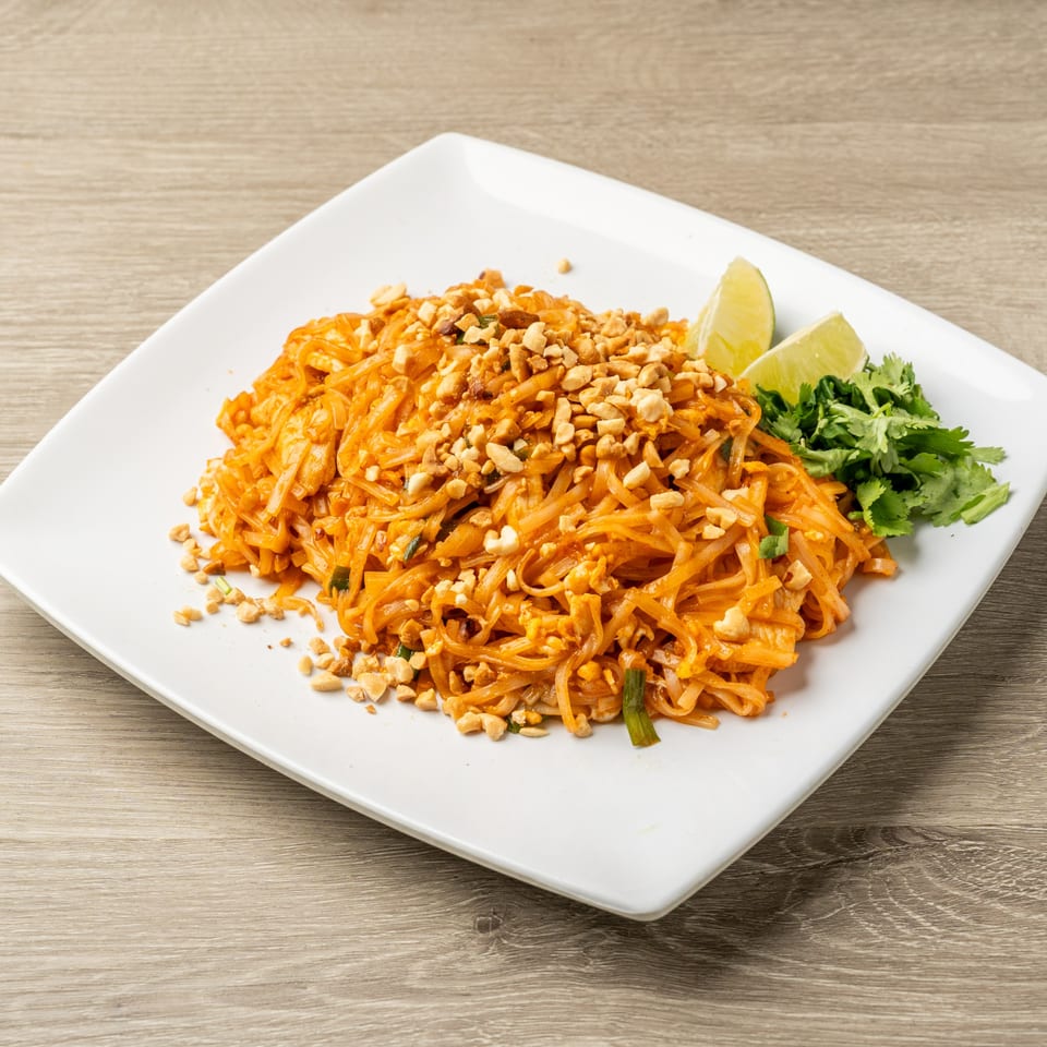 A plate of Tasty Thai's Pad Thai, garnished with crushed peanuts, lime wedges, and cilantro.